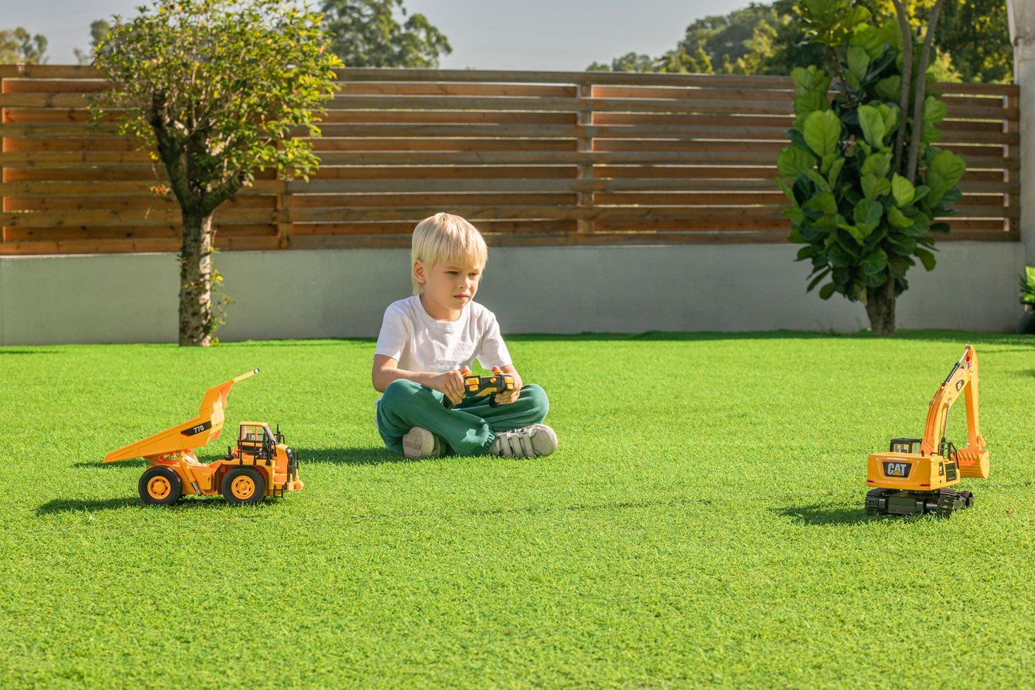 Young child with blonde hair playing with a toy dump truck on a lush green lawn, showcasing a product photo session.