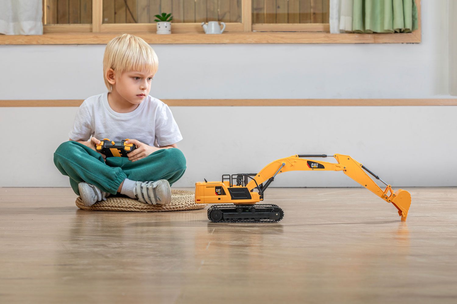 Young boy sitting on a mat indoors, focused on playing with a toy excavator, captured during a product photo shoot.