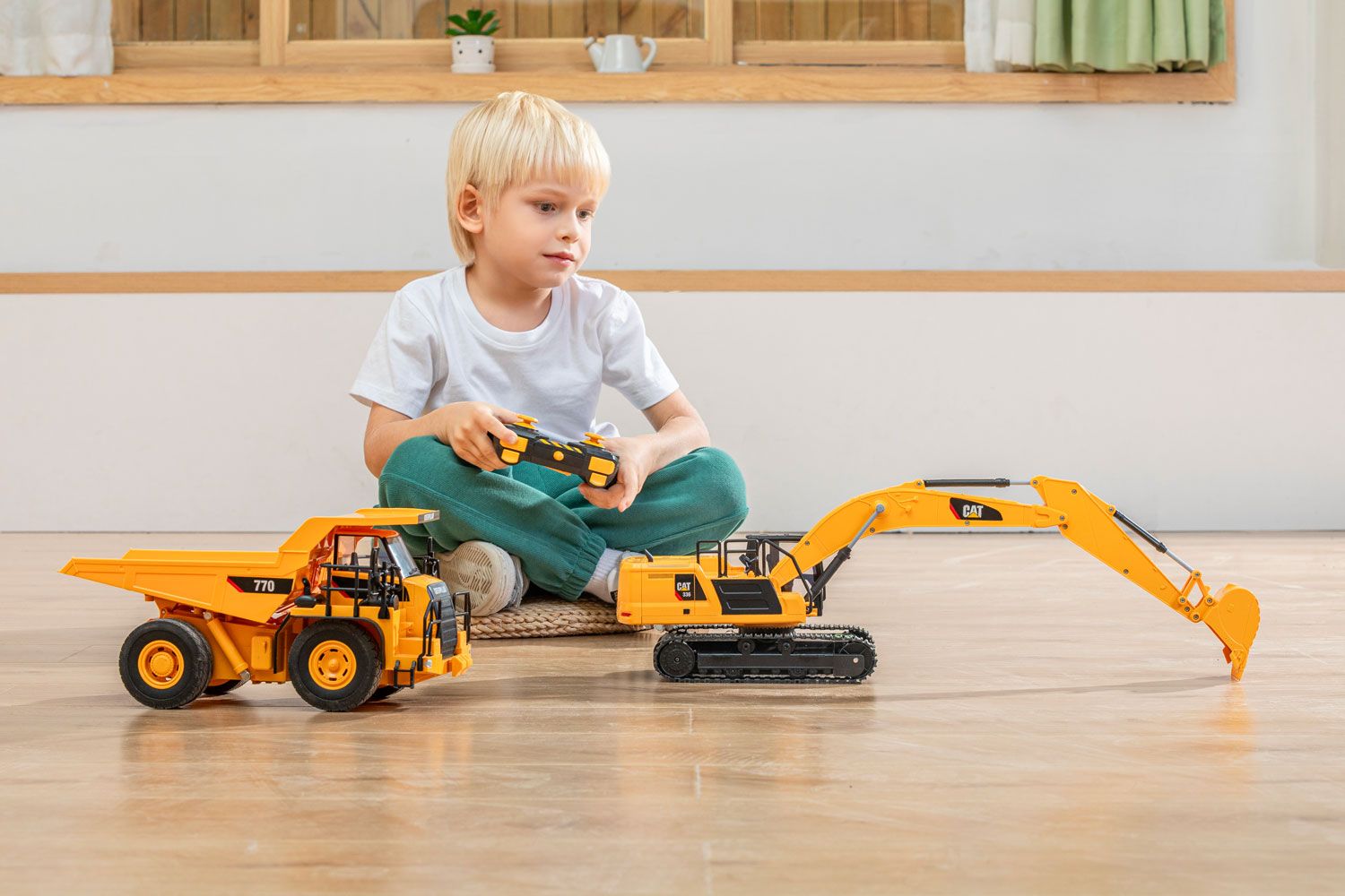 Blonde child in green pants and white shirt playing with a toy dump truck and excavator on a wooden floor, product photography example