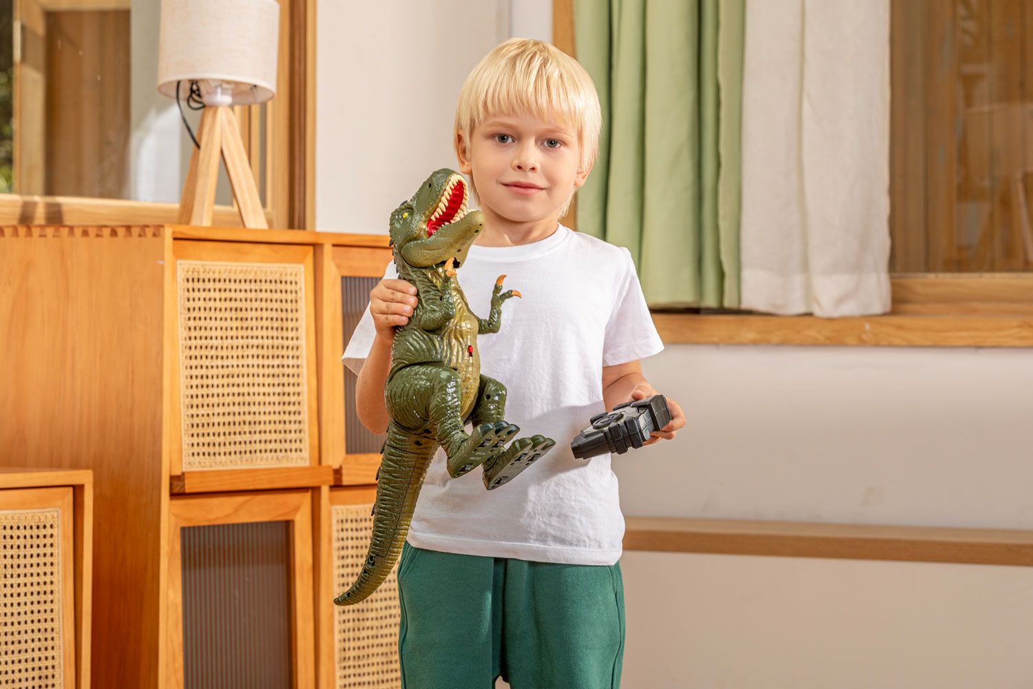 Child holding a toy dinosaur and remote control, with a happy expression, in a well-lit indoor setting for product photography.