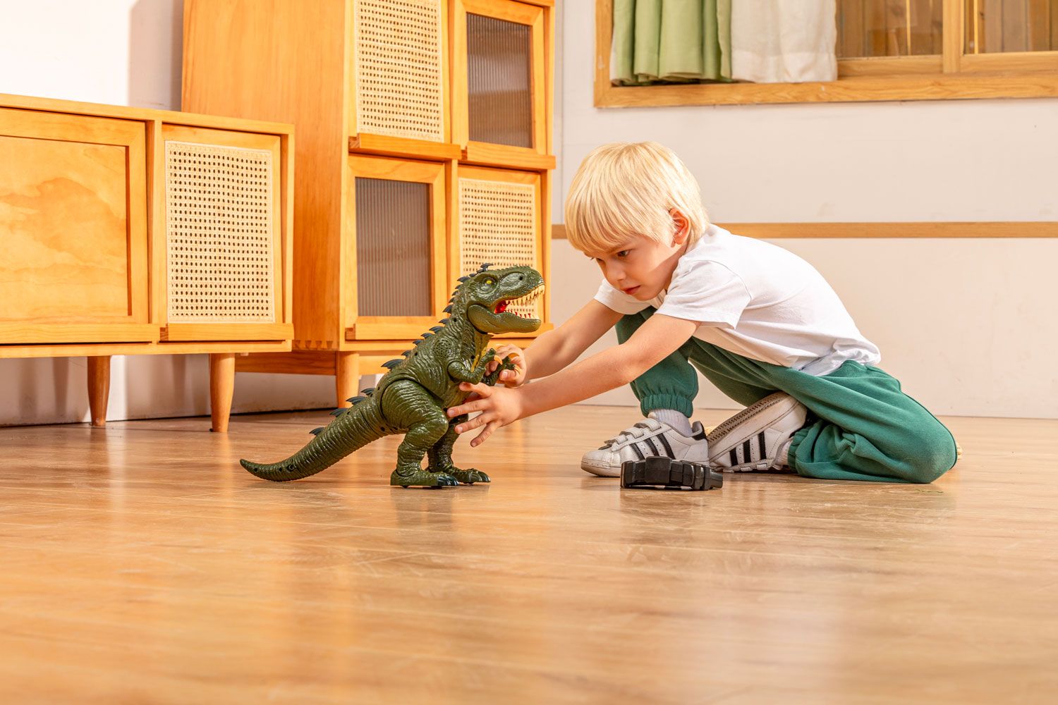 A young child with blonde hair crouching on a wooden floor, carefully playing with a toy dinosaur, displaying focus and enjoyment.