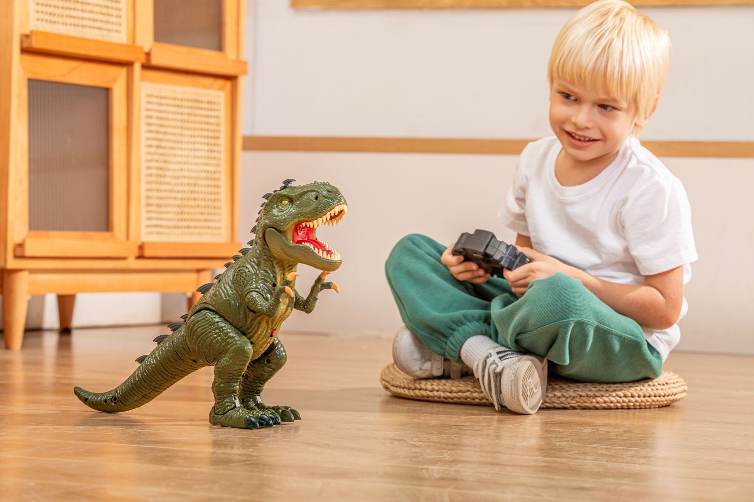 Smiling child sitting cross-legged on a wooden floor, holding a remote control with a toy dinosaur poised as if in motion, illustrating dynamic play.